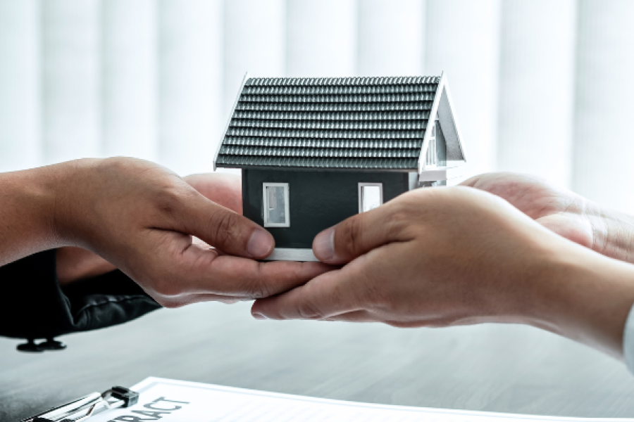 Duas pessoas a trocar uma casa miniatura com o logotipo Maxfinance 